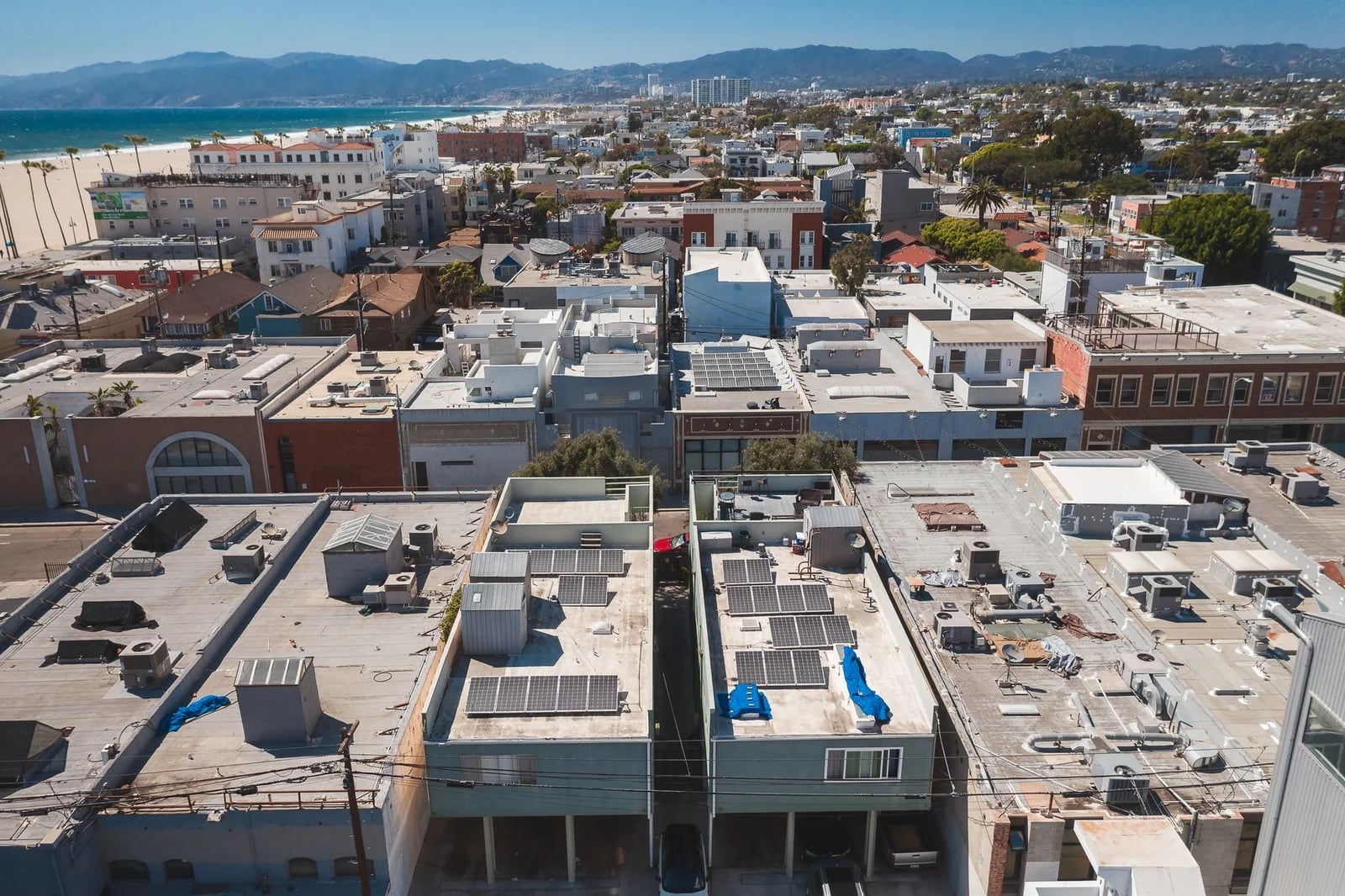 Drone view of a coastal urban area with rooftops and solar panels under a clear blue sky.